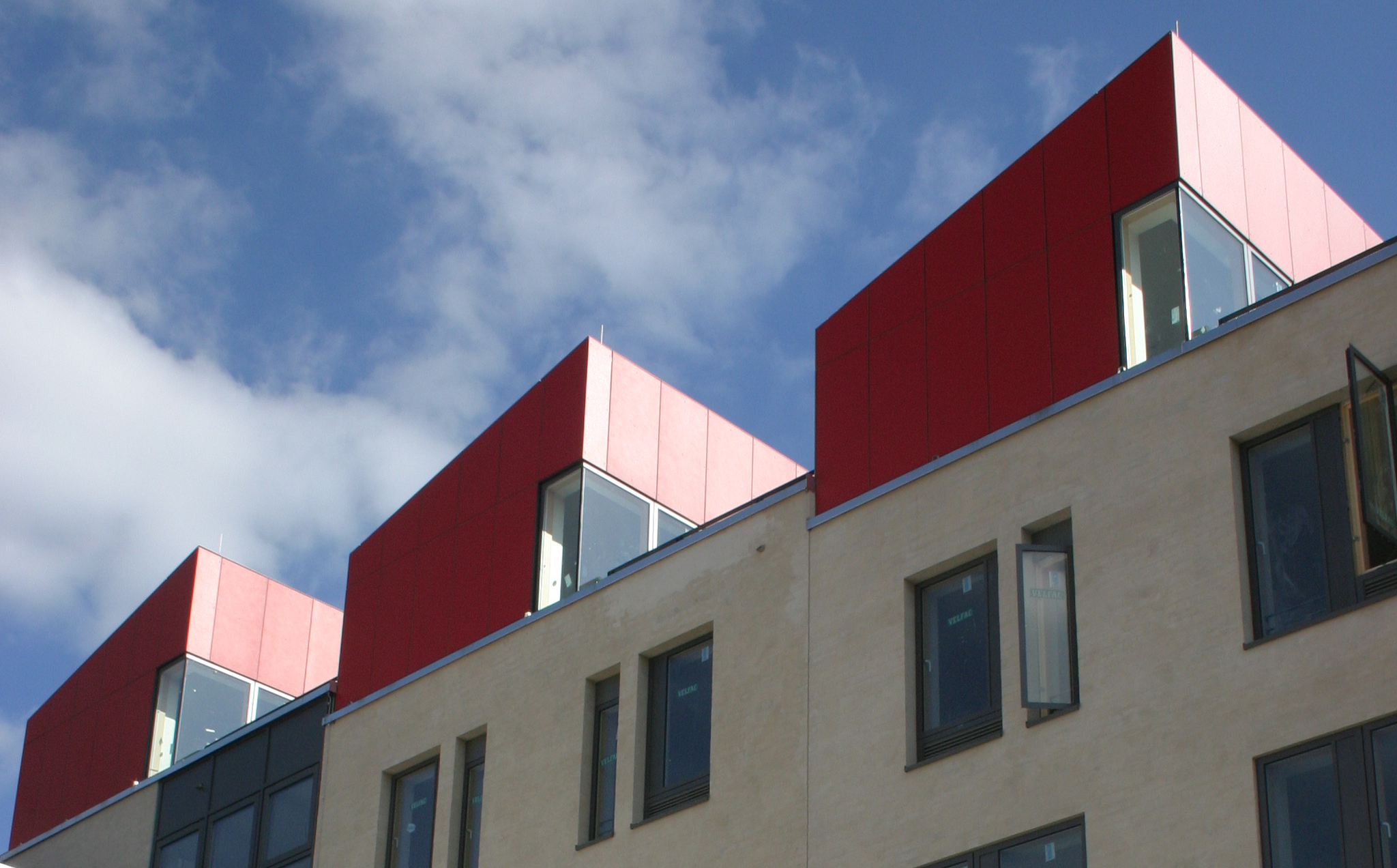 Ein Bild von der weißen Fassade des Studentenwohnheims Schleswig Holstein und den einzelnen Dachgeschoss-Wohnungen des Wohnheims, deren Fassade rot ist.